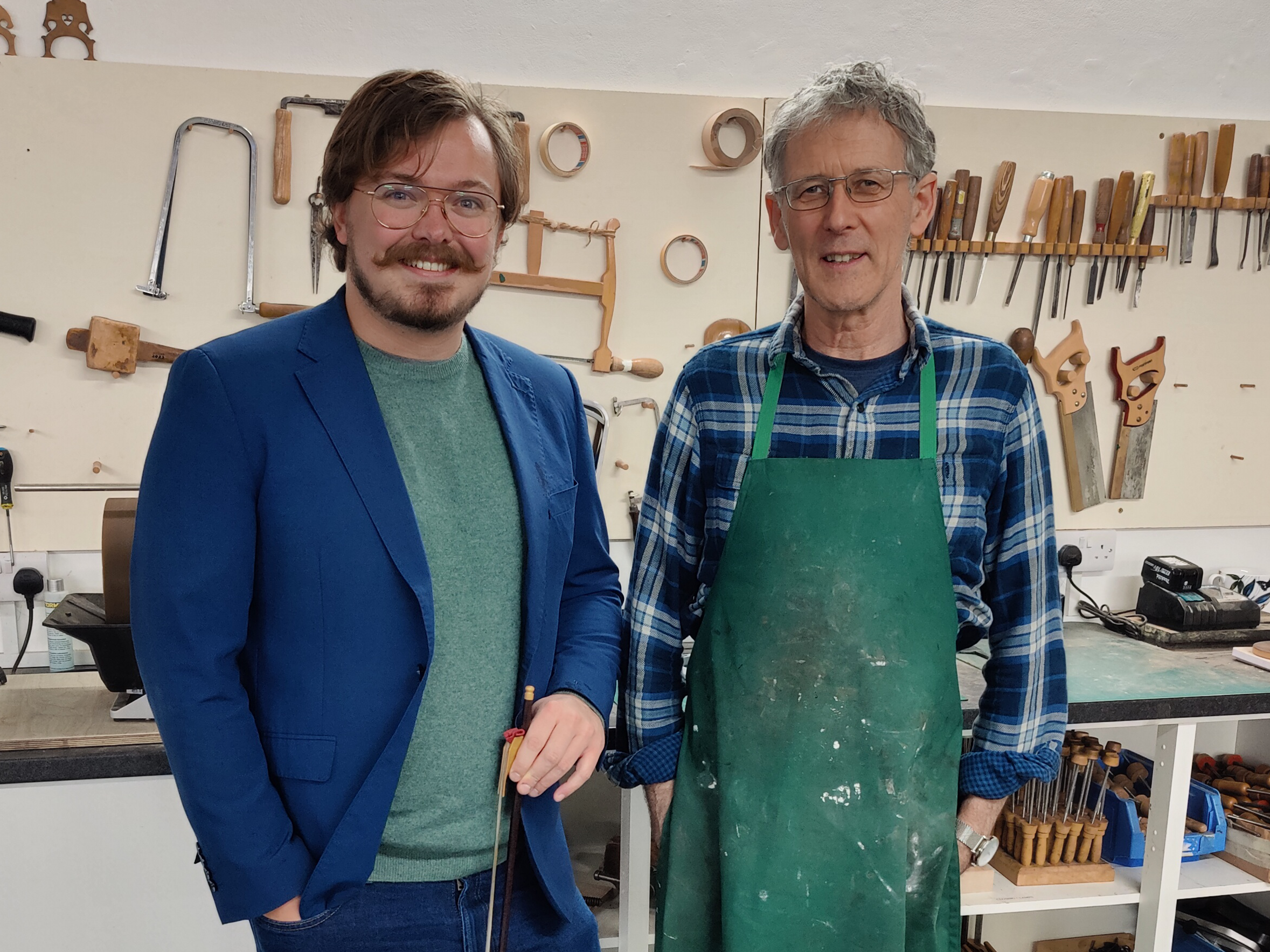 Image of two men – Fraser and Shem – stood next to each other in a workshop with tools behind them. Both are smiling.