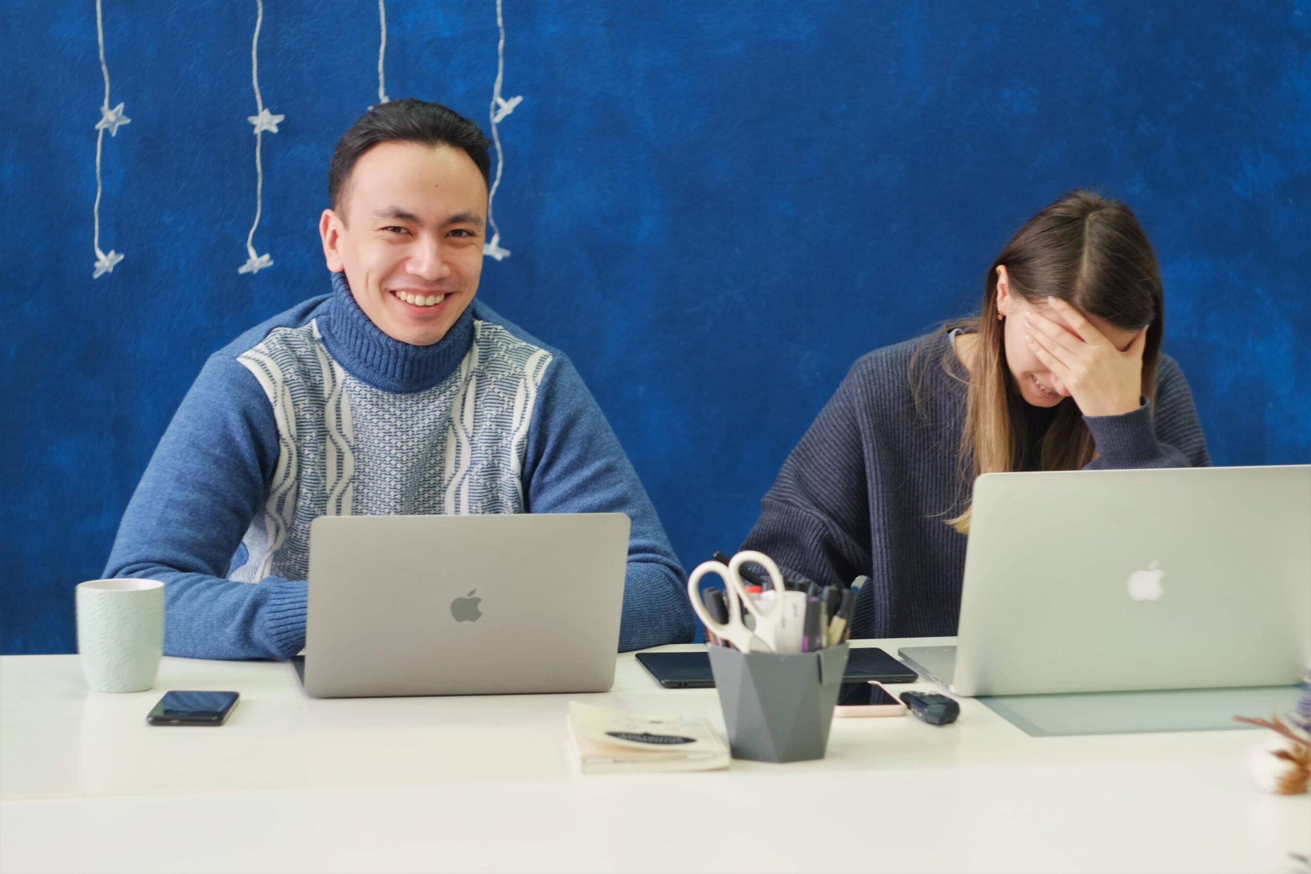Two businesspeople are interviewing for a cultural fit. Man on the left is grinning happily from behind a laptop, woman on the right has her hand over her head and looks to be breaking out with laughter. Image by Aleksandra Sapozhnikova