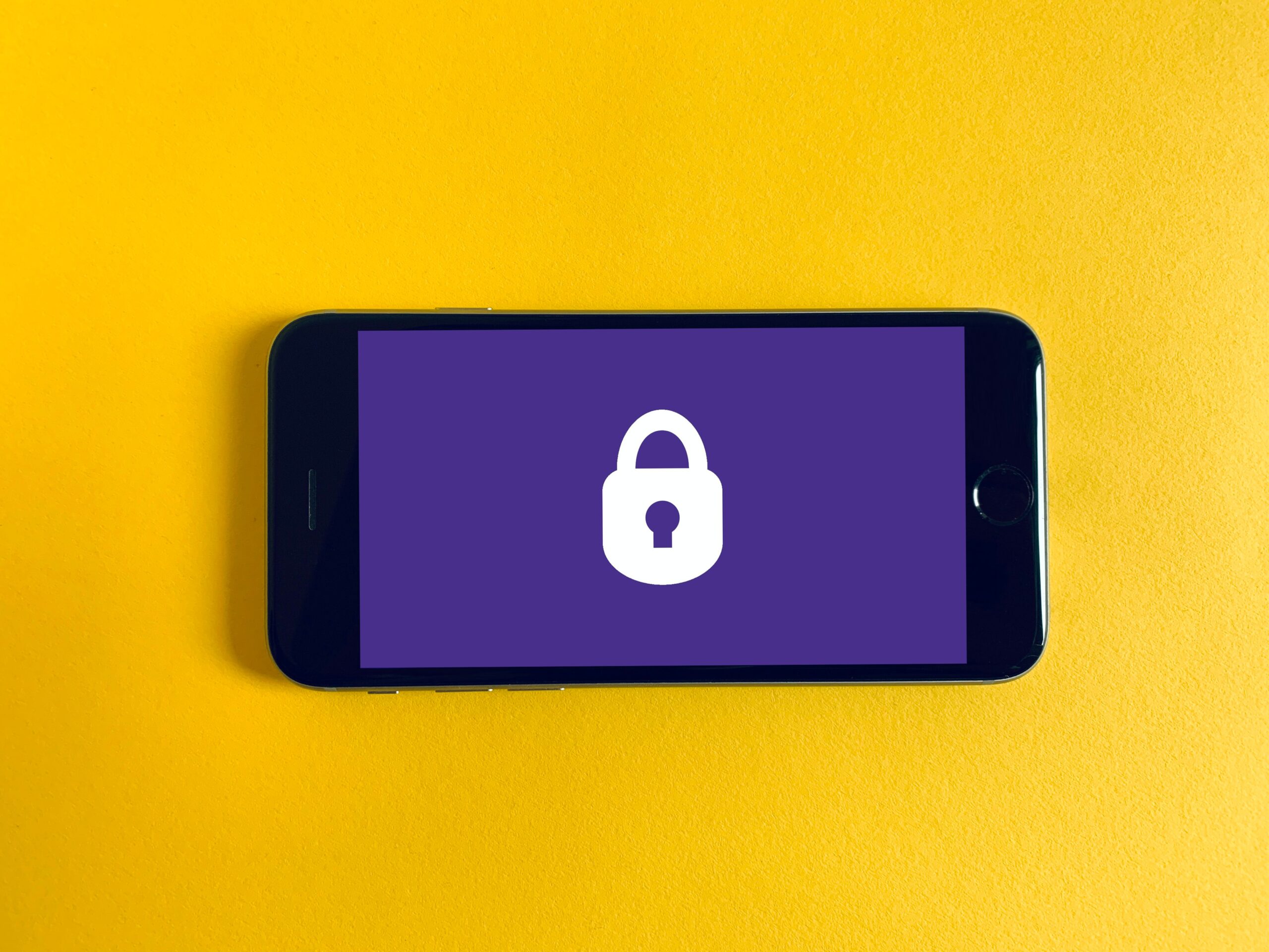 Survey anonymity is represented by a phone displaying a white padlock layered on a purple background. The phone is resting on a bright yellow surface. Image by franckinjapan.