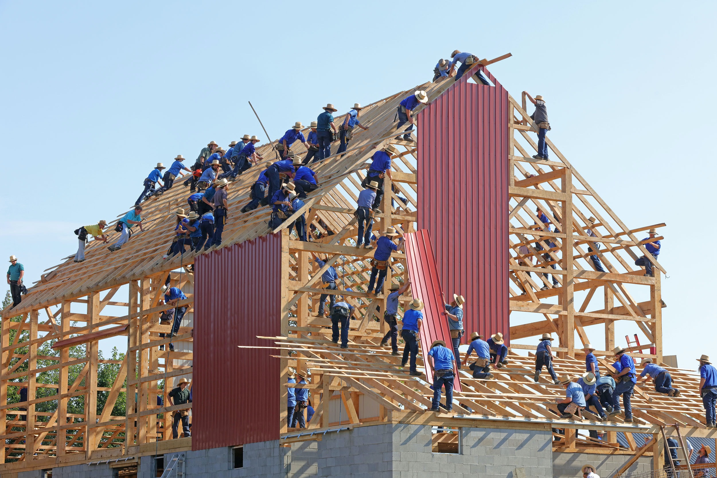 Image of a large group of people building a house together – all balanced on a wooden structure putting red panels onto it. This represents a culture of employee engagement. Image by Randy Fath on Unsplash.